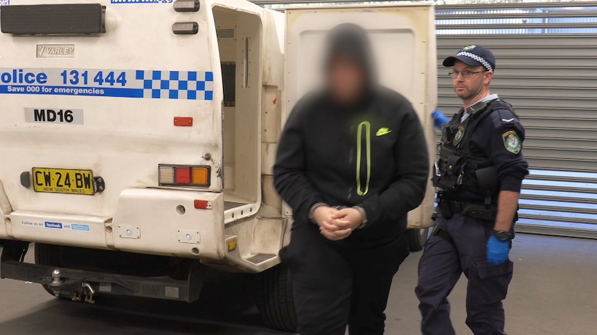 A man wearing a hoodie with a police officer standing next to police van