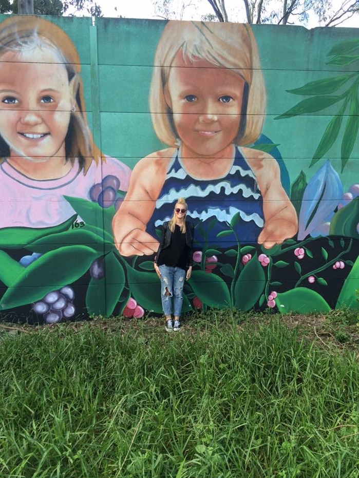 A woman stands in front of a wall mural showing a child's face