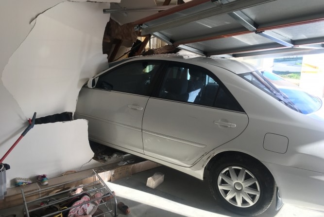 A car facing the wrong way in a garage, with its nose through a wall.