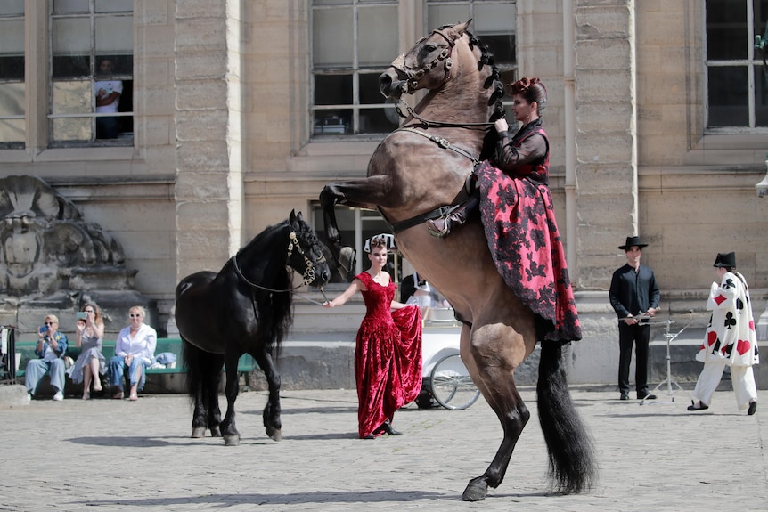 A trainer on a horse in a red dress, a second model wears a red dress leading another horse. 