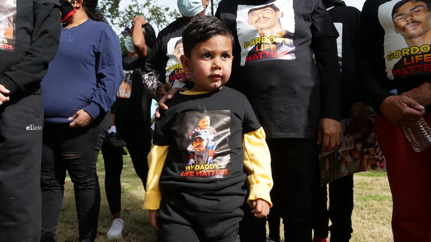 A small Aboroginal boy marches in a protest with other marchers around him. Most are wearing black with messages printed on them