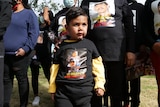 A small Aboroginal boy marches in a protest with other marchers around him. Most are wearing black with messages printed on them