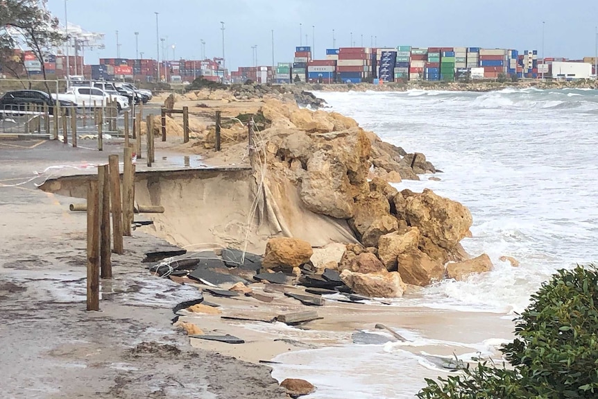 A badly eroded stretch of beach with a container port in the background.