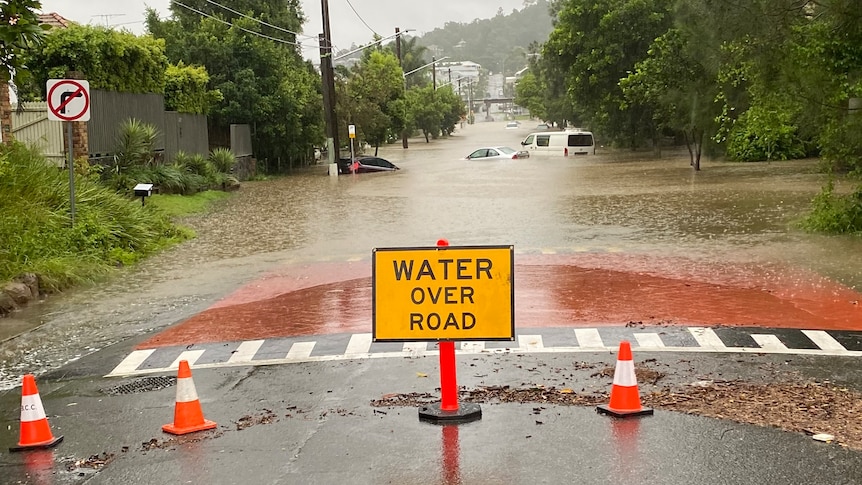 Flood warning sign on road, cars in water in flooded road behind in Brisbane street amid severe weather event