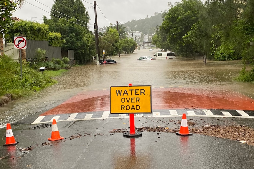 Flood warning sign on road, cars in water in flooded road behind in Brisbane street amid severe weather event