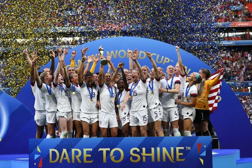 The US women's football team raise their arms and celebrate with their trophy