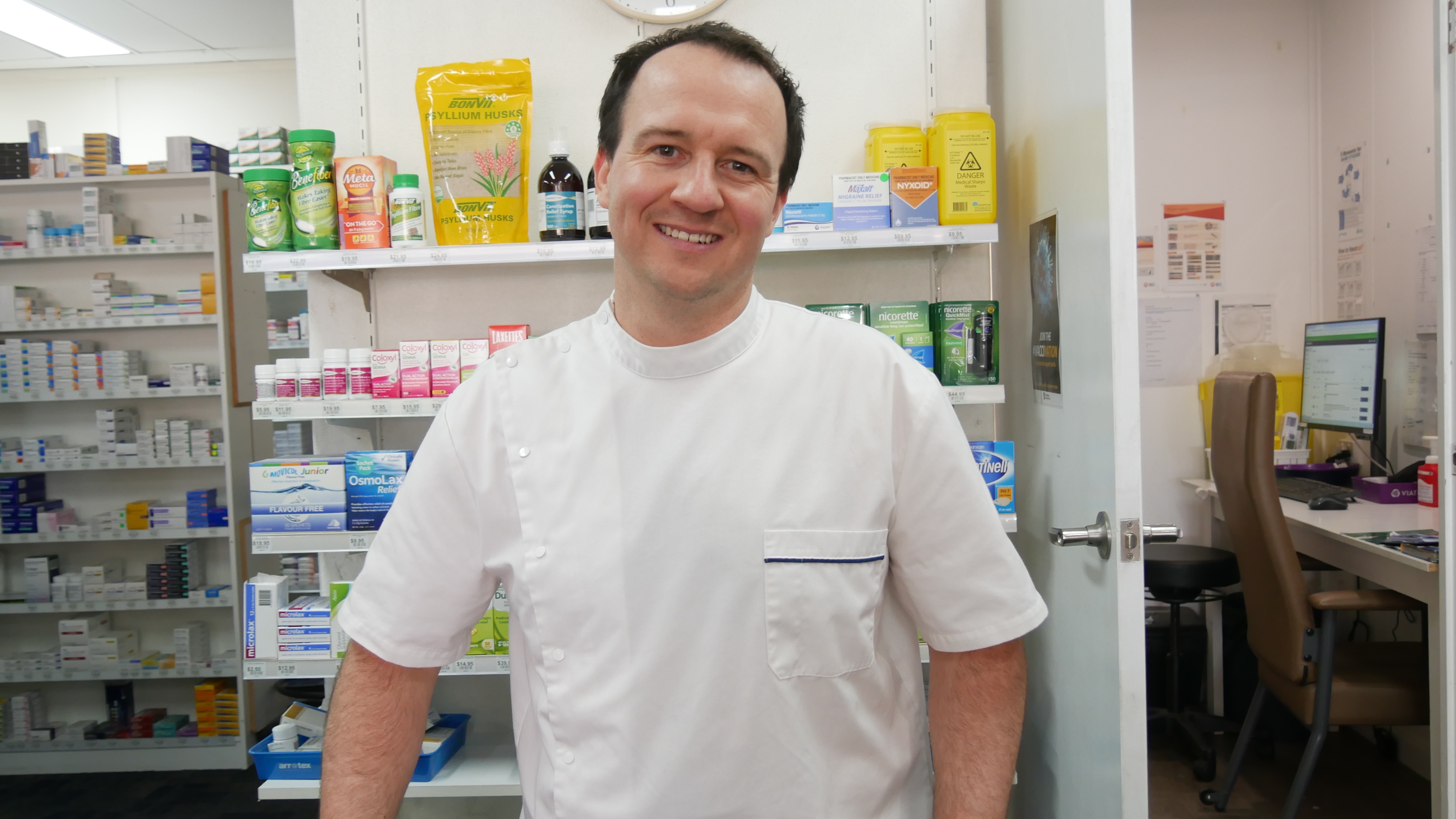 A man in a white shirt stands behind a counter smiling at the camera.