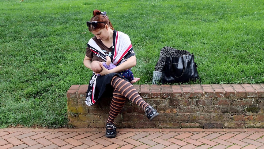 A breastfeeding mother sits in a park