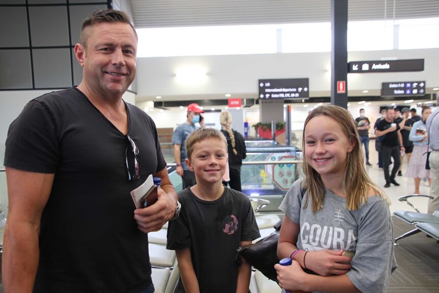 A father and his two children stand in the Perth Airport terminal posing for a photo.
