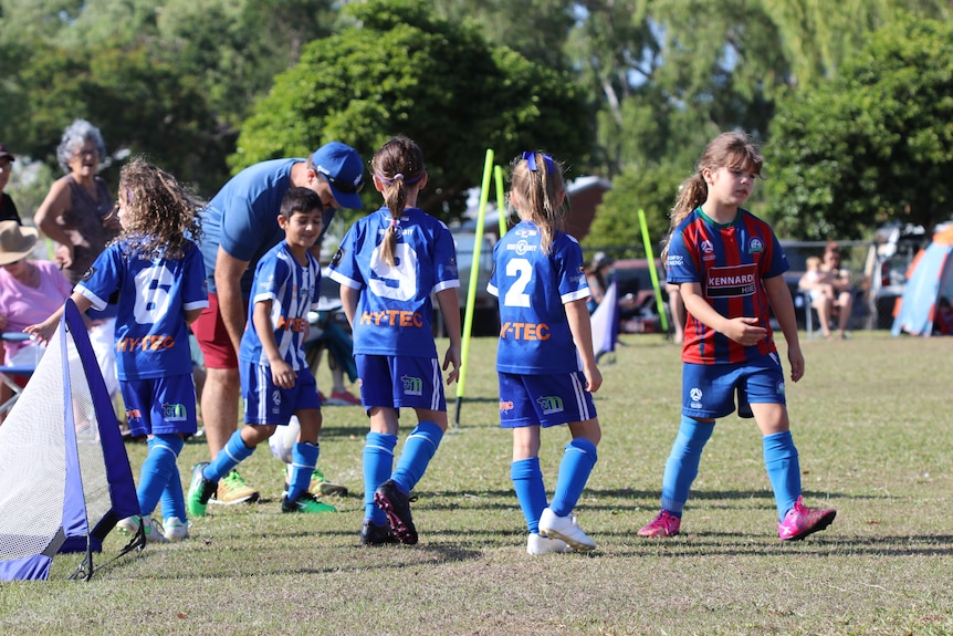 A team of junior soccer players gather on the field in the sun