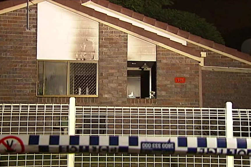 A brick low-set house with smoke damage at a window and police tape out the front.