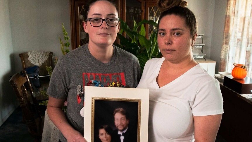Two young women hold a framed photo of their parents