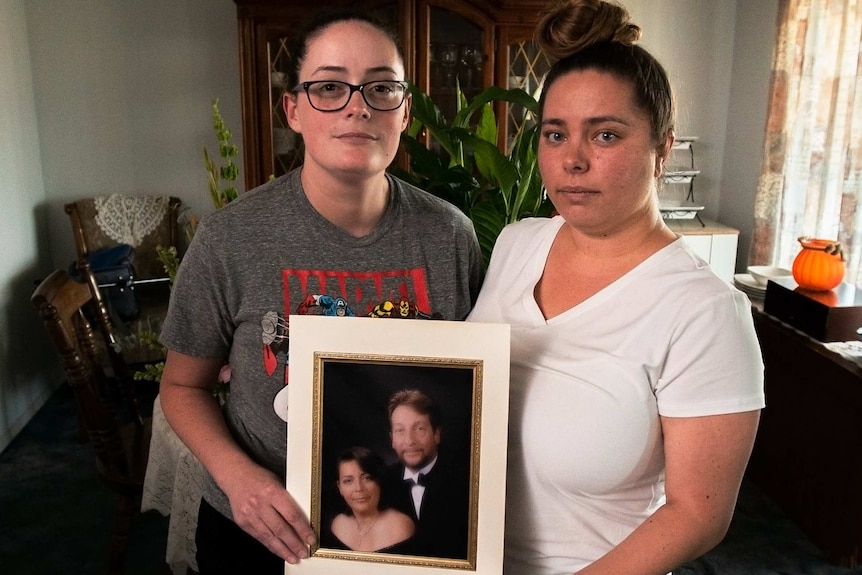 Two young women hold a framed photo of their parents