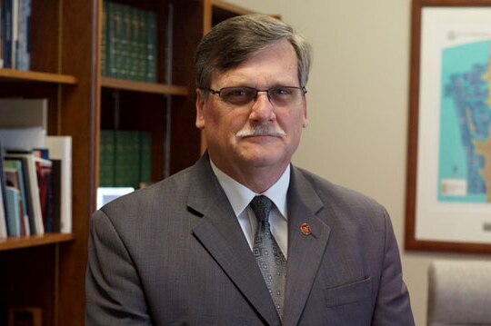 Simon O'Brien sits in his office, wearing a grey suit and tie.