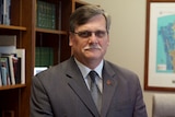 Simon O'Brien sits in his office, wearing a grey suit and tie.