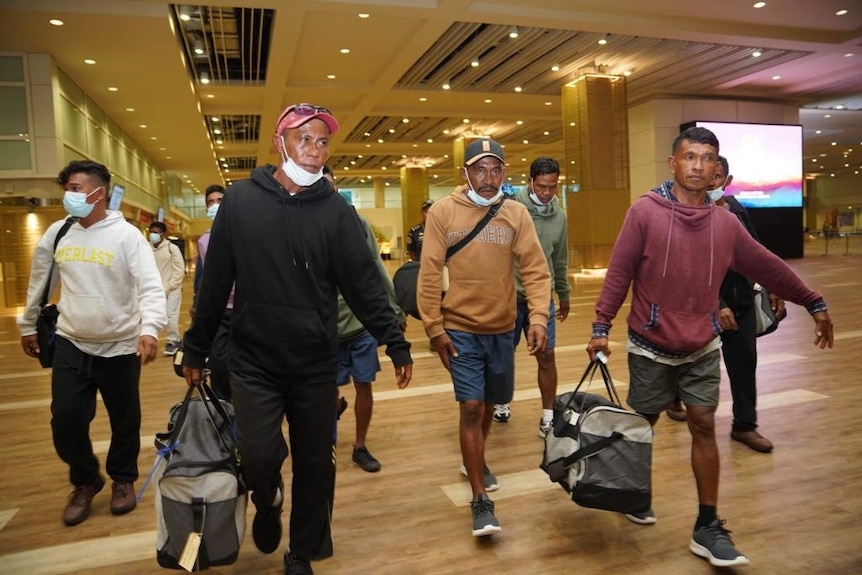 A group of Indonesian men walking through an airport with luggage 