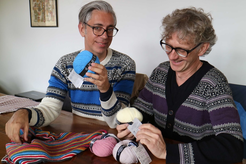 two men hold balls of knitting yarn