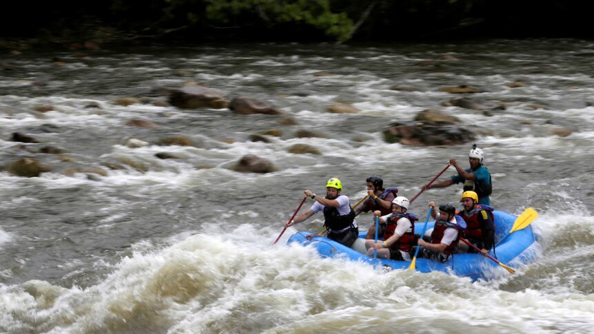 Five people and their guide, who are wearing helmets and life jackets, prepare to navigate a rapid in an inflatable raft.
