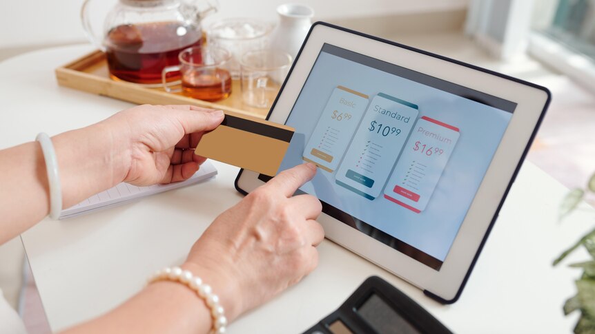a womans hands hold a credit card and select a subscription plan on an ipad