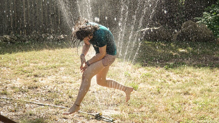 Woman runs through a sprinkler in backyard