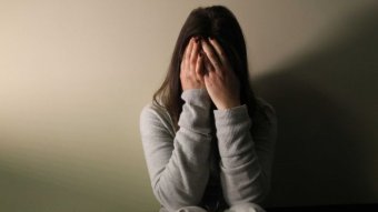 A woman covering her face and sitting on the floor upset.