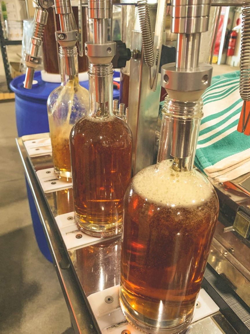 Caramel-coloured alcohol being poured into glass bottles.