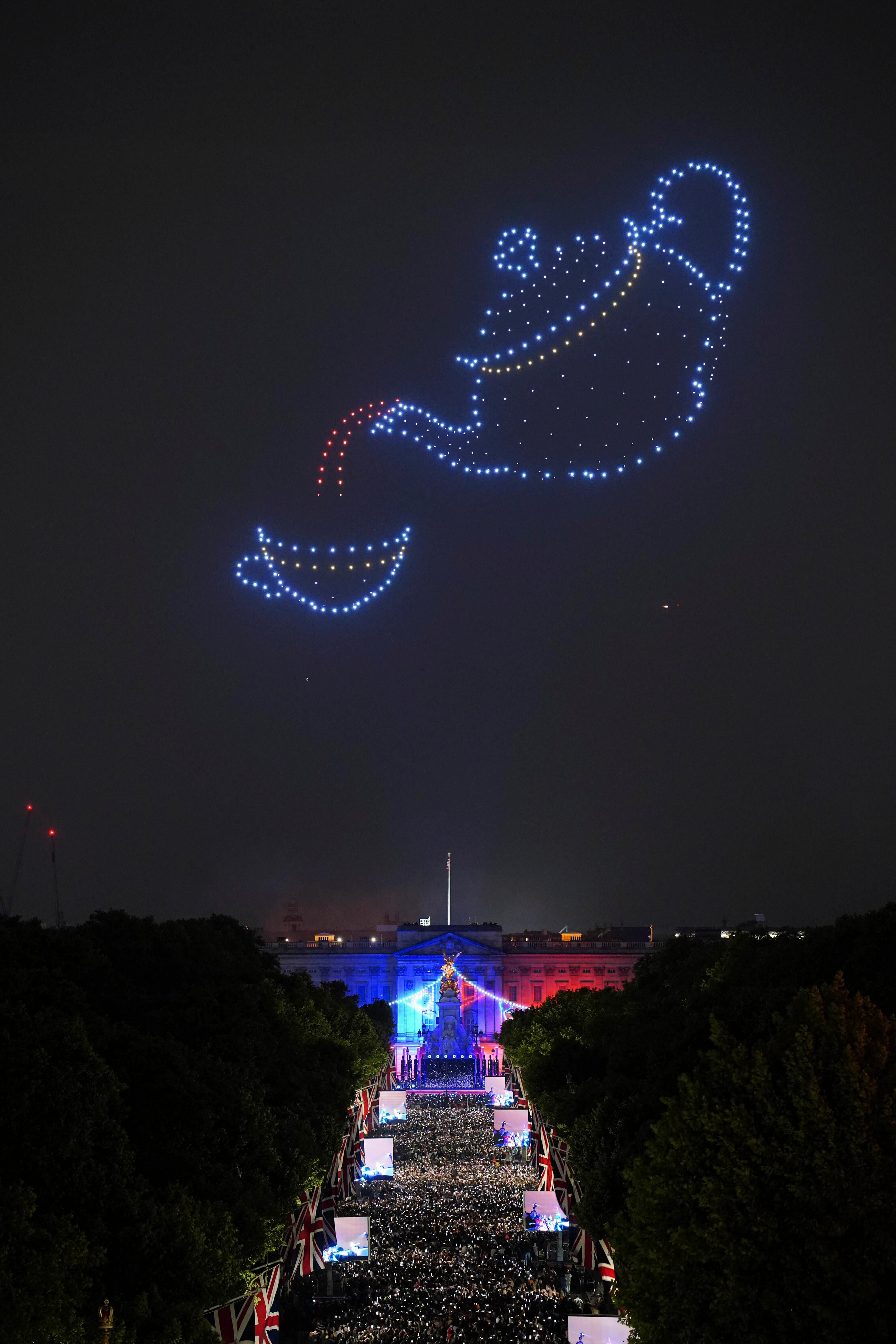 Drones with blue and red lights form the shape of a teapot and teacup above Buckingham Palace