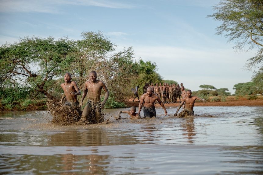 A group of boys run through a river.