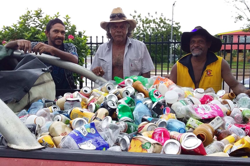 Three men lean against a ute filled with cans.