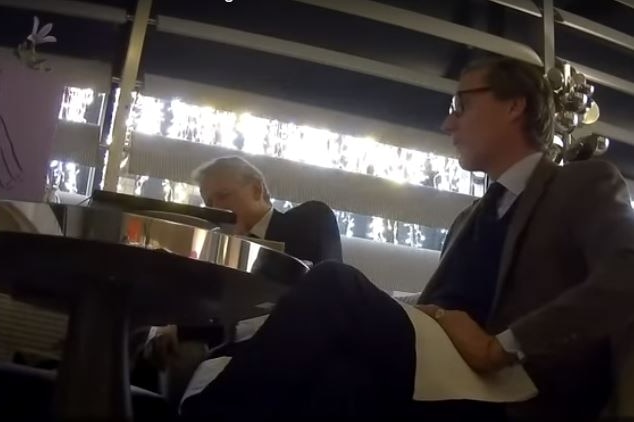 Hidden camera still of Alexander Nix sitting at a table next to another man.
