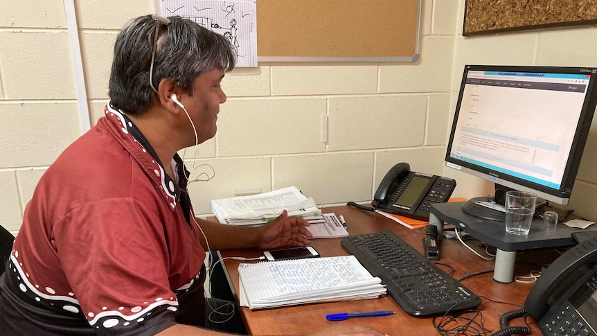 A male staff member of the Northern Territory Custody Notification Service is seated at a desk while working on a computer.