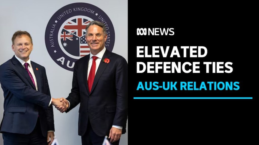 Elevated Defence Ties, Aus-UK Relations: Australian and UK Defence Ministers shake hands in front of the AUKUS logo.