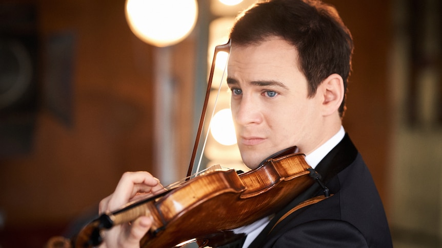 Violinist Jack Liebeck playing violin against a blurred background of stage lights