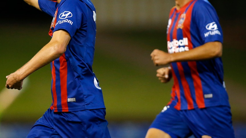 A Newcastle Jets player vies for possession against a Brisbane Roar opponent.