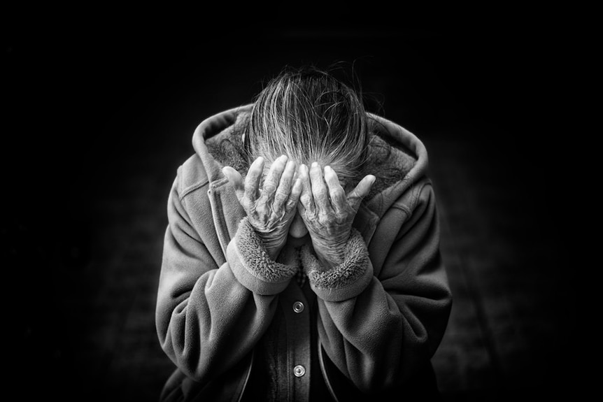 A older woman puts her head in her hands.