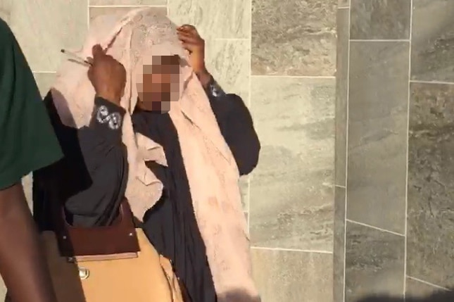 Mother unidentified, walking out of court holding a scarf over her face.