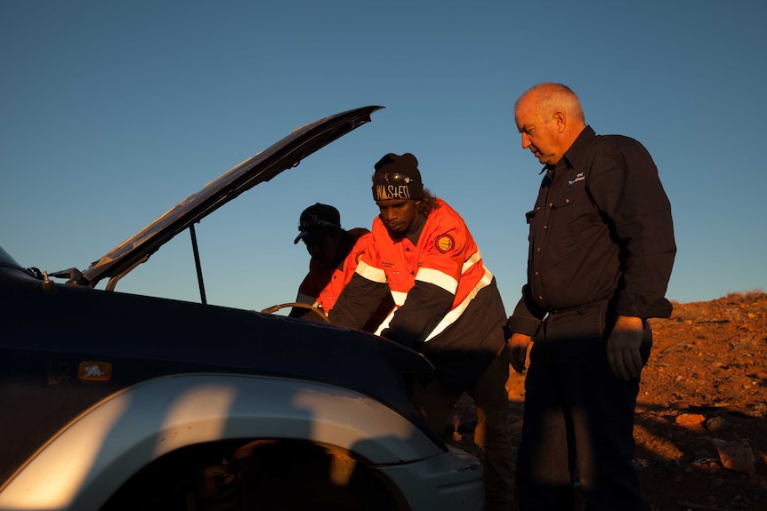 Three men look for car parts in a car graveyard outside Wiluna