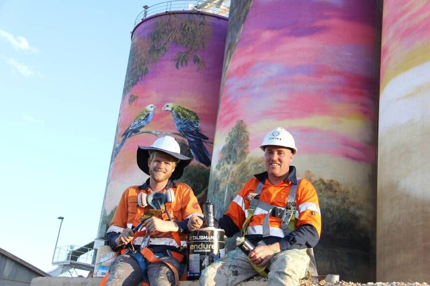 Two artists in high vis clothing in front of a half painted silo