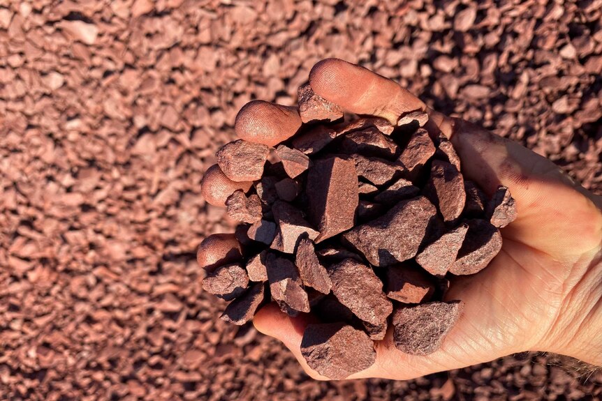A man is holding a handful of iron ore in the NT.