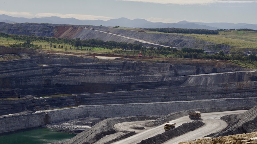 An open cut coal mine in the hunter region of new south wales. There are large mining trucks driving into the pit.