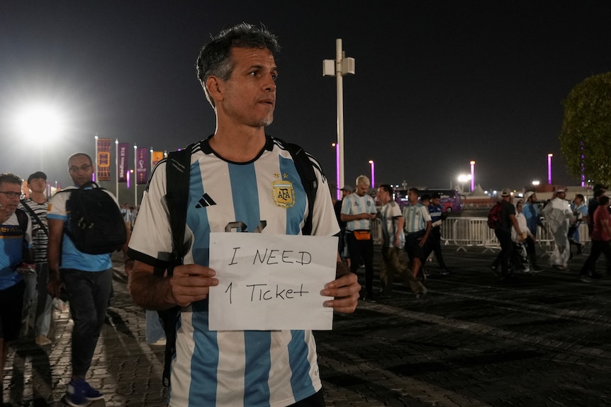 A man in a Morocco jersey holds a sign saying 'I need 1 ticket'. 