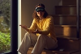 A woman sitting on a staircase, wearing augmented reality goggles. 