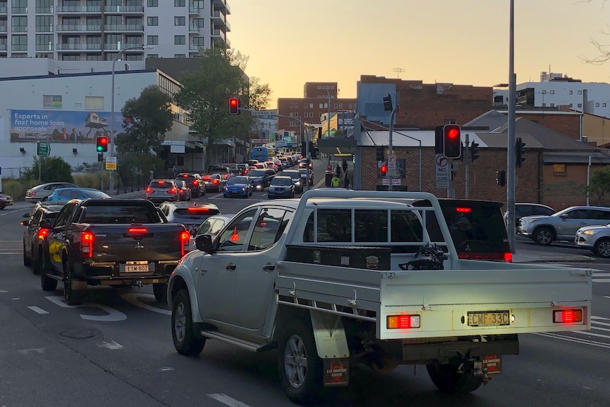 A lot of cars wait in line at a set of traffic lights at dusk.