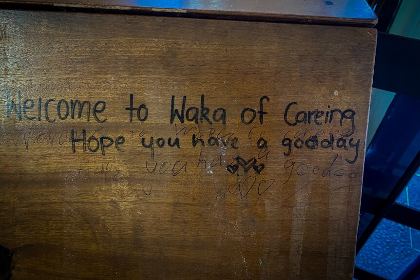 A wooden cupboard with writing on it, which reads 'Welcome to Waka of Careing. Hope you have a gooday' (sic)