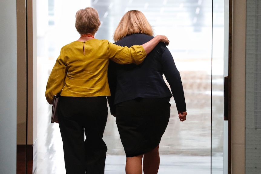 Helen Haines, earing a mustard yellow shirt walking out of the chamber with her arm around Bridget Archer