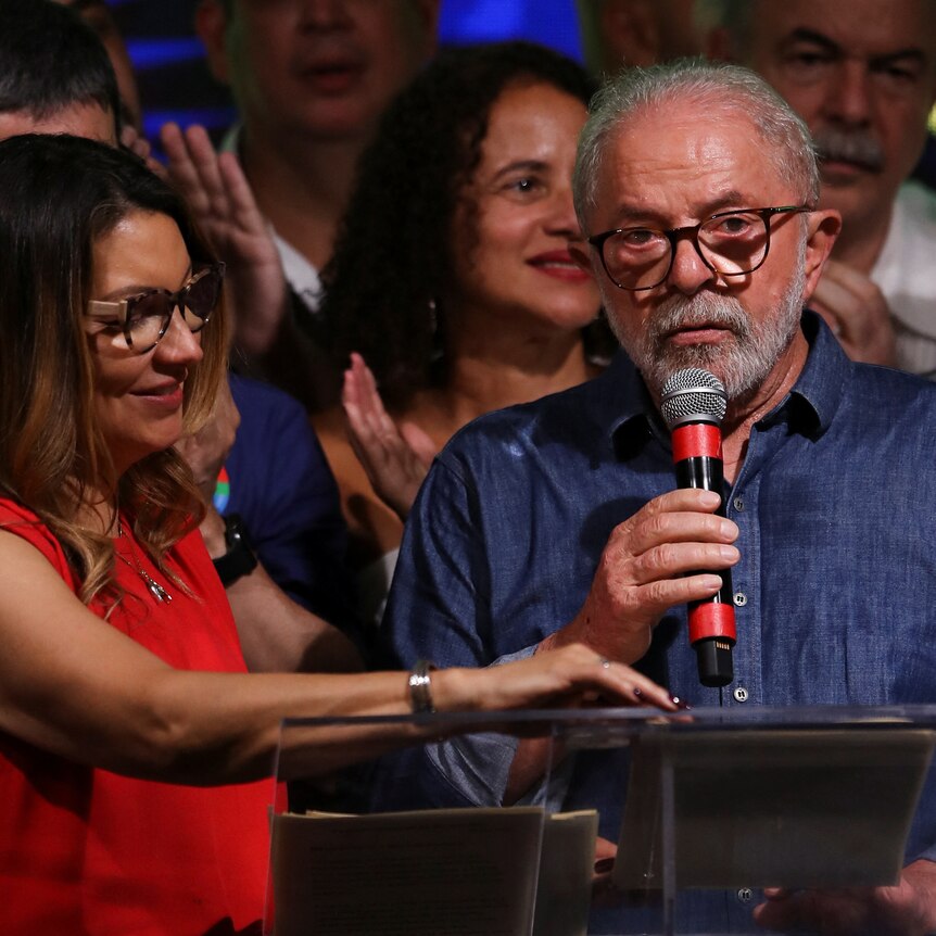 Luiz Inacio Lula da Silva speaks with a microphone up to his mouth, next to his wife Rosangela Lula da Silva.