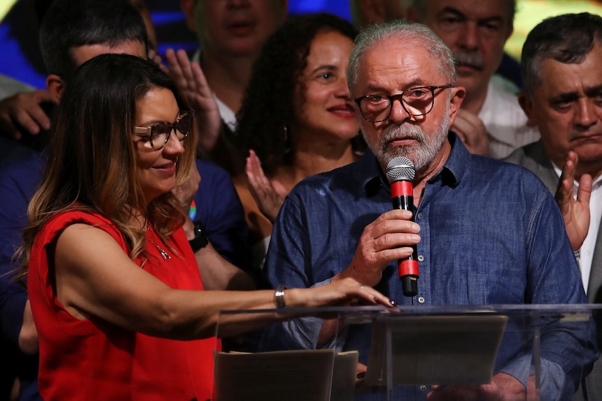 Luiz Inacio Lula da Silva speaks with a microphone up to his mouth, next to his wife Rosangela Lula da Silva.