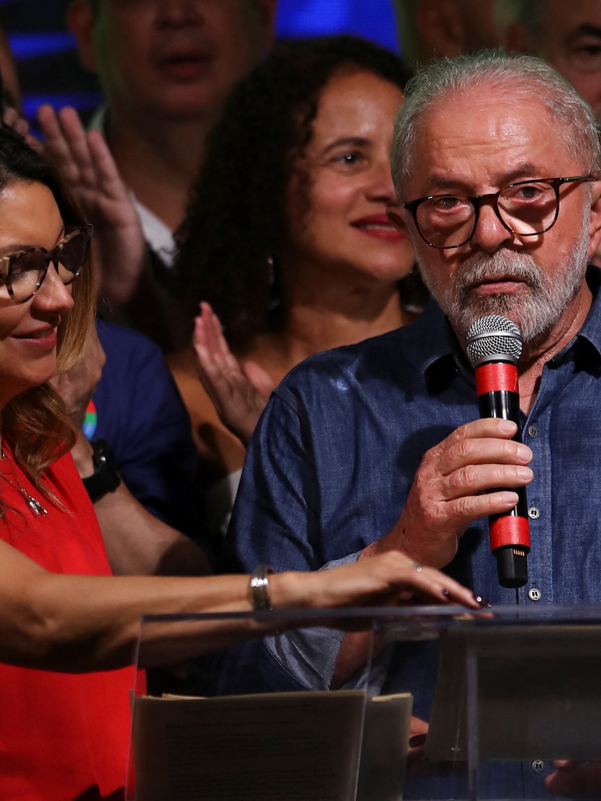 Luiz Inacio Lula da Silva speaks with a microphone up to his mouth, next to his wife Rosangela Lula da Silva.