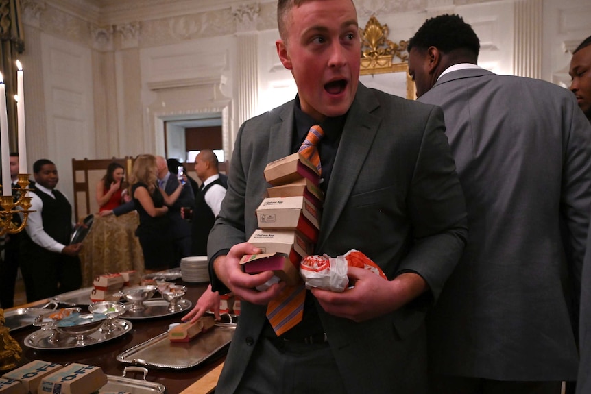 A Clemson Tigers player, wearing a suit, walks away from the table with four Big Macs and two Wendy's sandwiches.