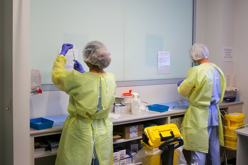 Two health workers in PPE drawing vials of coronavirus vaccine.